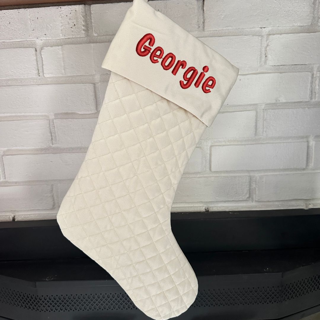 cream quilted stocking with embroidered name in red thread.