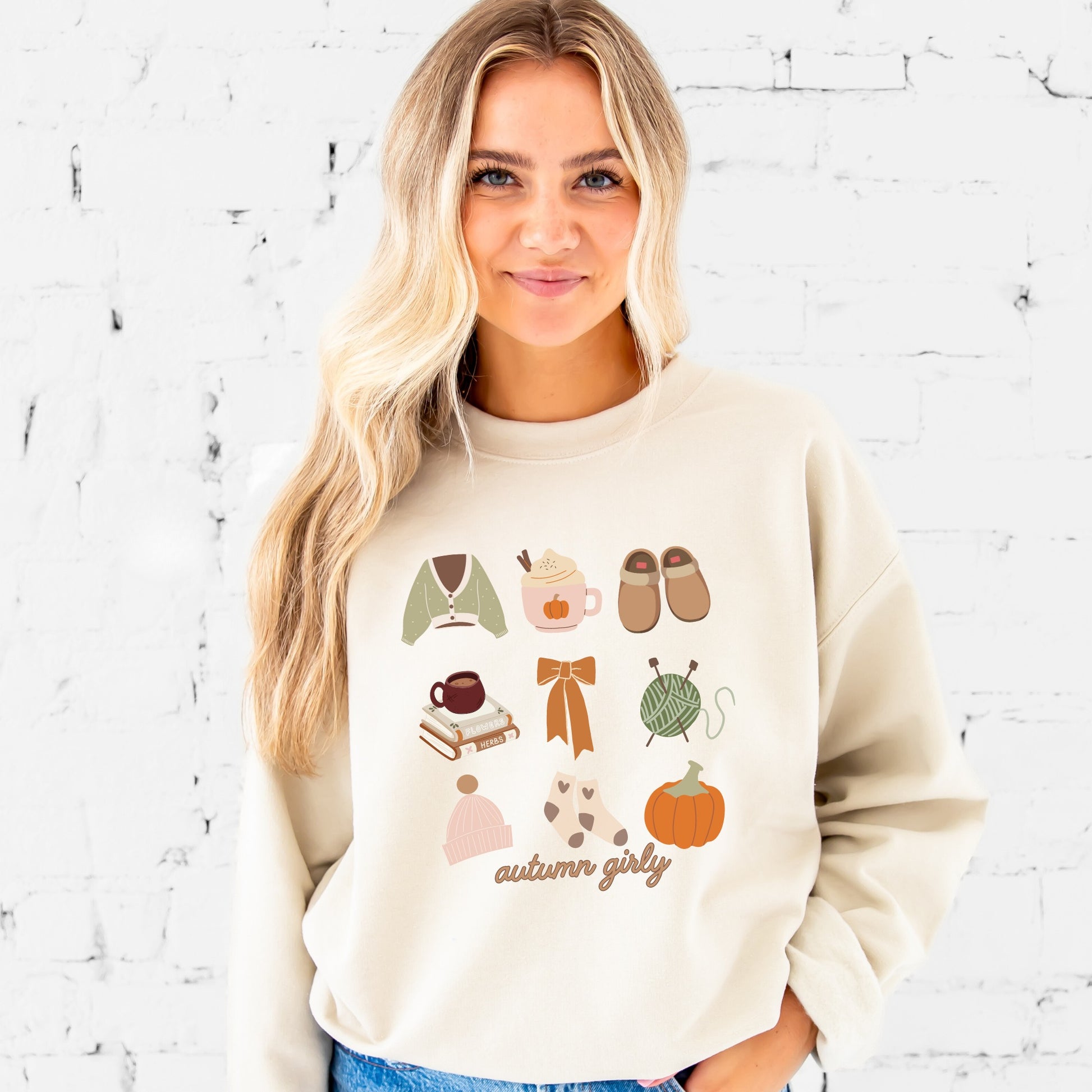 girl wearing a sand crewneck sweatshirt with cozy, autumn girly fall icons printed in a grid style, including the following: sweater, pumpkin spice, slippers, books, bow, yarn, hat, socks, pumpkin