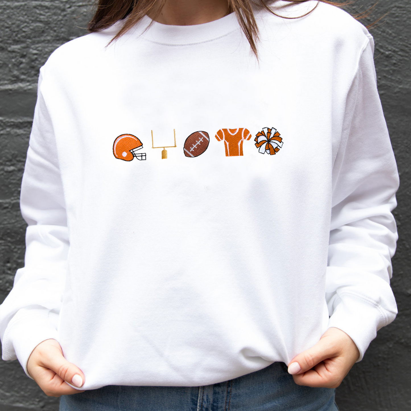 close up of a woman wearing a white crewneck sweatshirt with embroidered football icons in orange thread