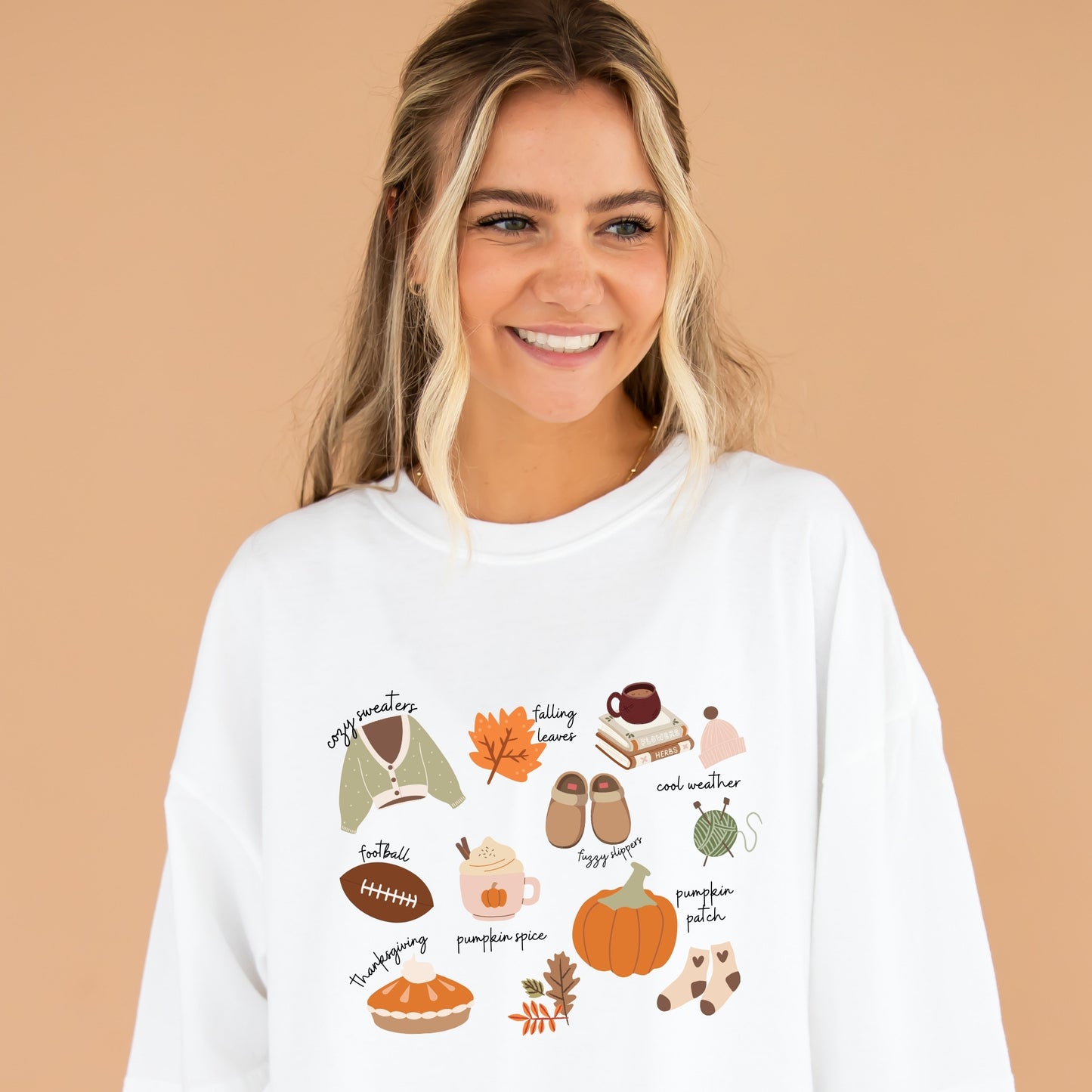 Girl wearing an oversized white comfort colors t-shirt with cute fall inspired icons including a sweater, falling leaves, a stack of books, knitting needles and thread, pumpkin spice latte, socks, pumpkin pie, and a football