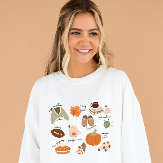 Girl wearing an oversized white comfort colors t-shirt with cute fall inspired icons including a sweater, falling leaves, a stack of books, knitting needles and thread, pumpkin spice latte, socks, pumpkin pie, and a football