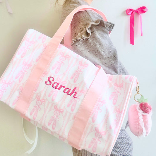 Pink floral blanket with 'Sarah' embroidered, surrounded by baby clothes and a pink bow.