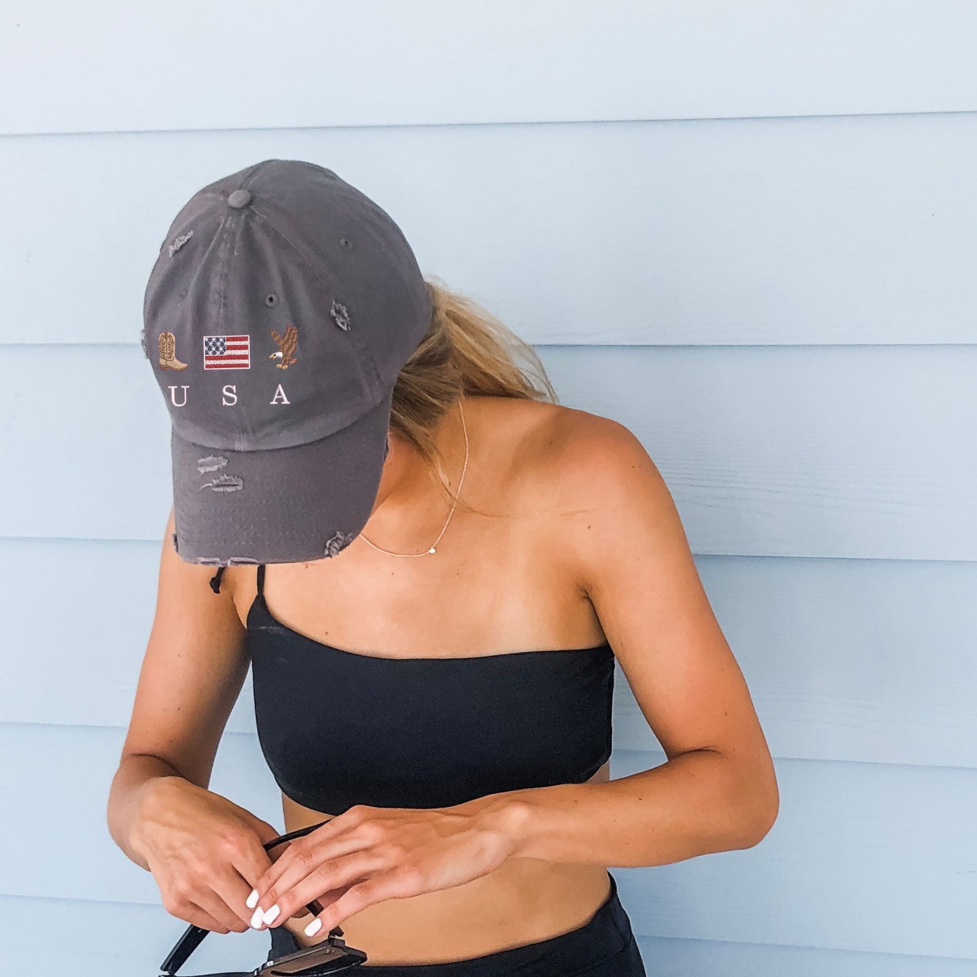 woman wearing a nickel distressed baseball cap with embroidered cowboy boot, american flag, eagle, and USA design