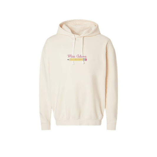 an ivory lightweight comfort colors hooded pullover with a custom name embroidered over an embroidered pencil icon on the center front of the shirt