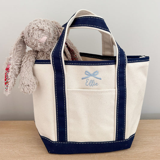 small open top mini canvas tote bag with navy trim and and custom name and mini bow embroidery in powder blue thread