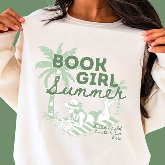 close up of a woman wearing a sweet cream sweatshirt with large green printed Book Girl Summer design featuring palm trees, a girl laying out on a stripped beach towel reading a book and text that says book girl summer and plot twists and tan lines.