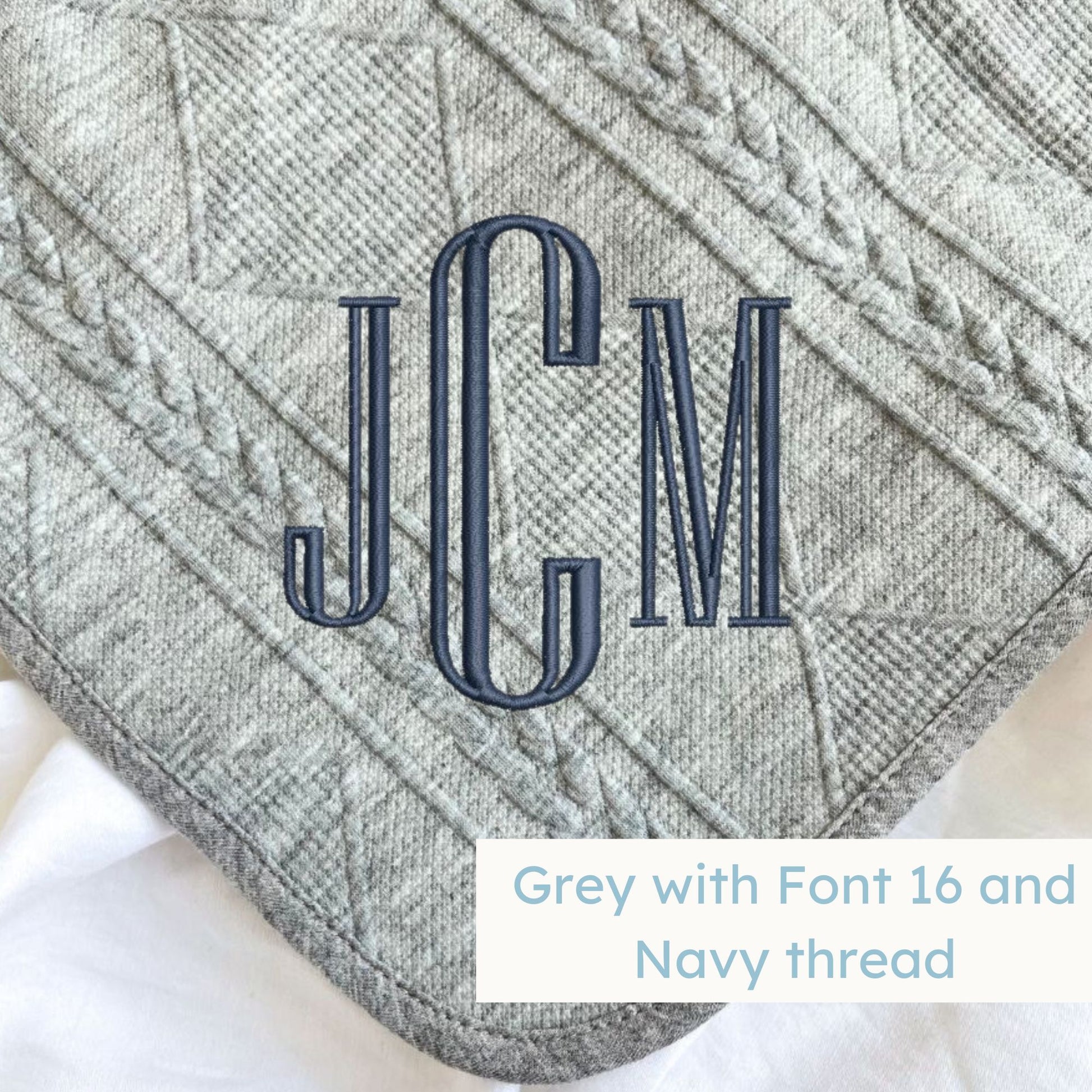 A grey knitted blanket with a personalized monogram embroidered on the corner