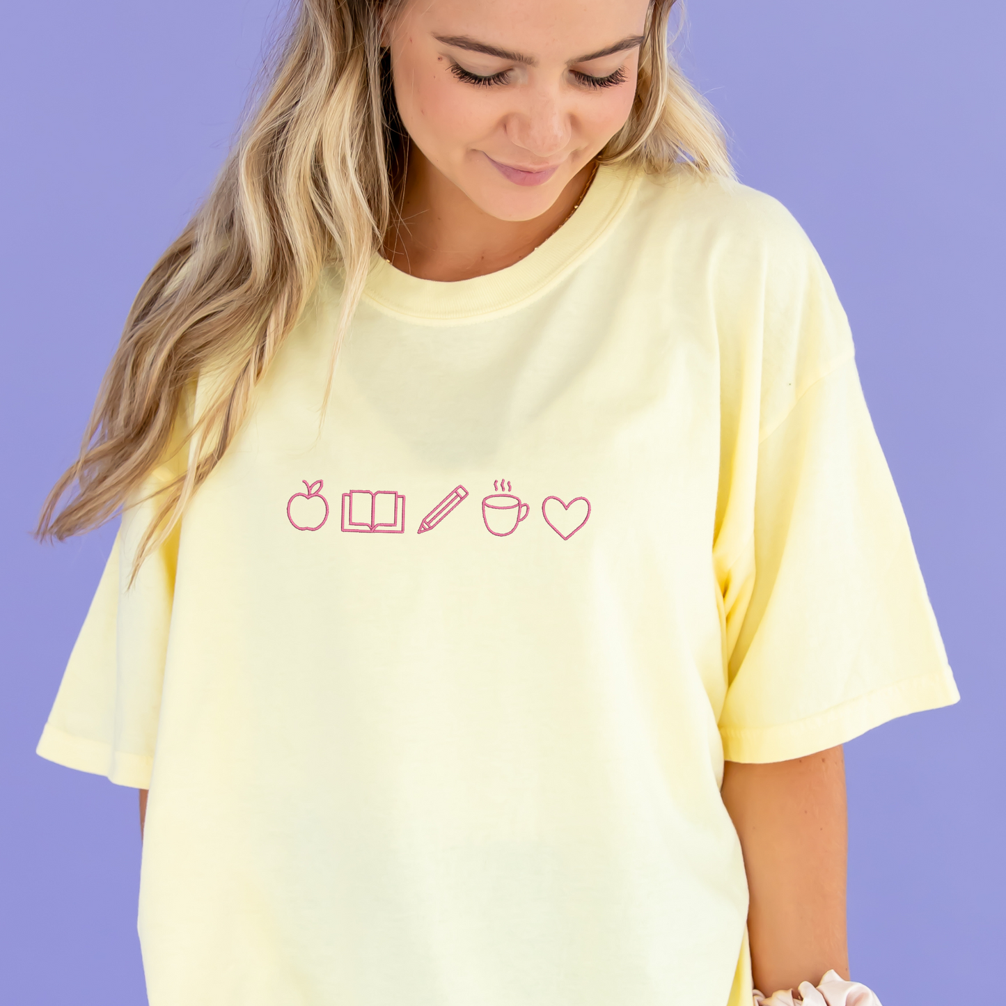 young woman wearing a banana tee with embroidered teacher icons in pink thread across the chest