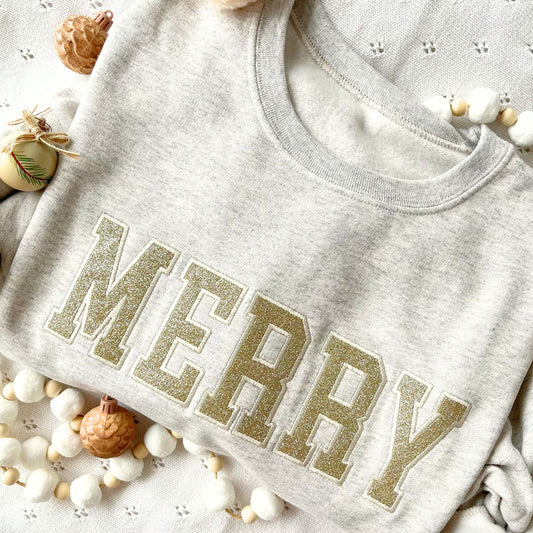 heather oatmeal crewneck with a sparkly gold merry design embroidered design across the chest