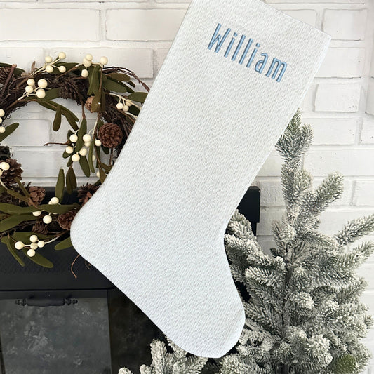 white and silver Christmas stocking with custom embroidered name in handicraft font and powder blue thread