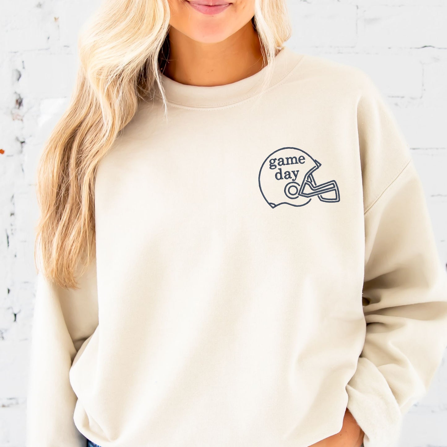 woman wearing a sand crewneck with embroidered game day and football helmet on the left chest in navy thread