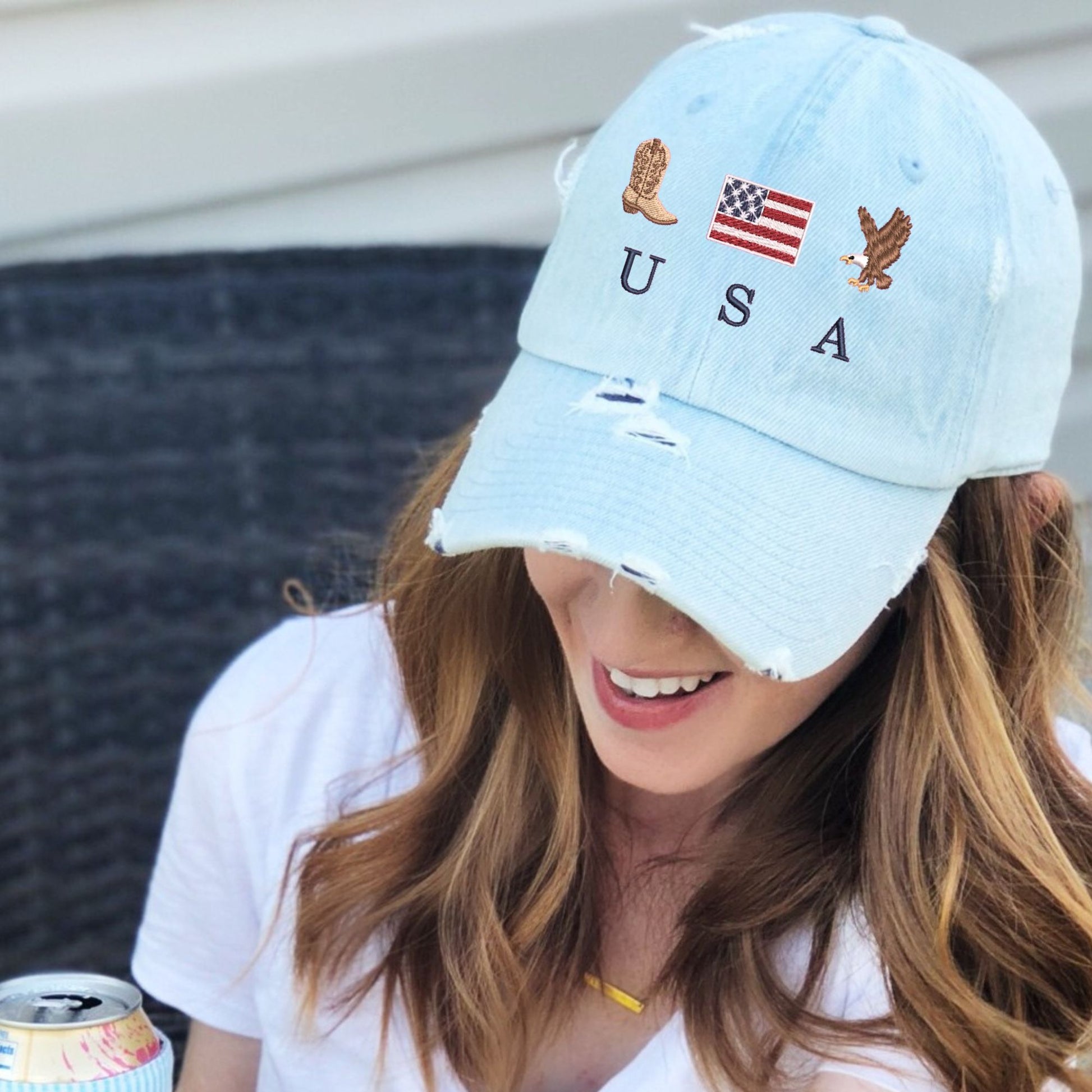 woman wearing a light denim distressed baseball cap with embroidered cowboy boot, american flag, eagle, and USA design