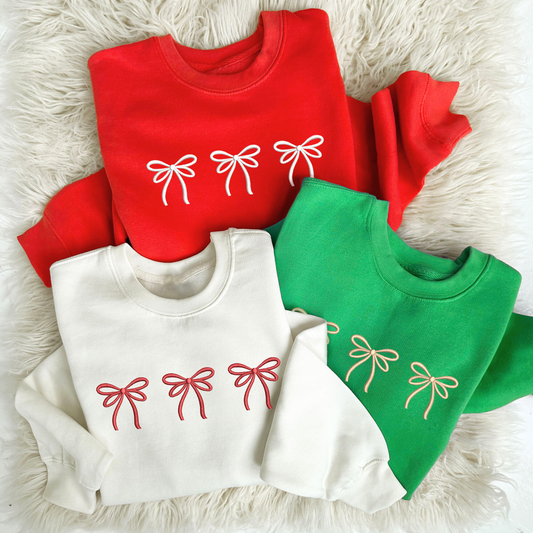 flat lay of 3 youth crewneck in red, kelly green, and white with three embroidered bows across the chest in white, red and camel thread.