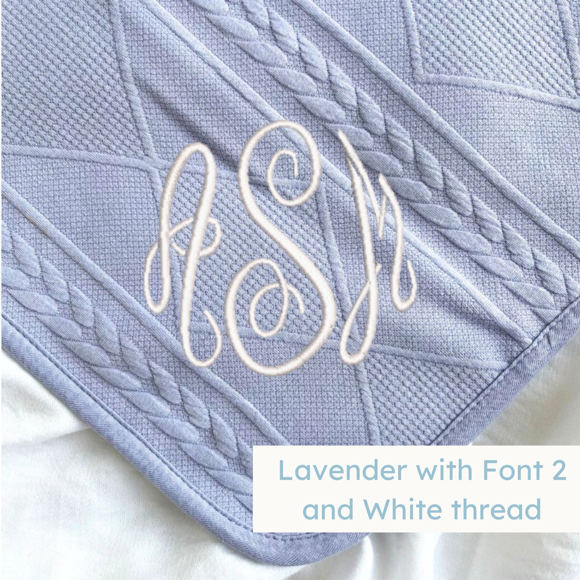 A lavender knitted blanket with a personalized monogram embroidered on the corner
