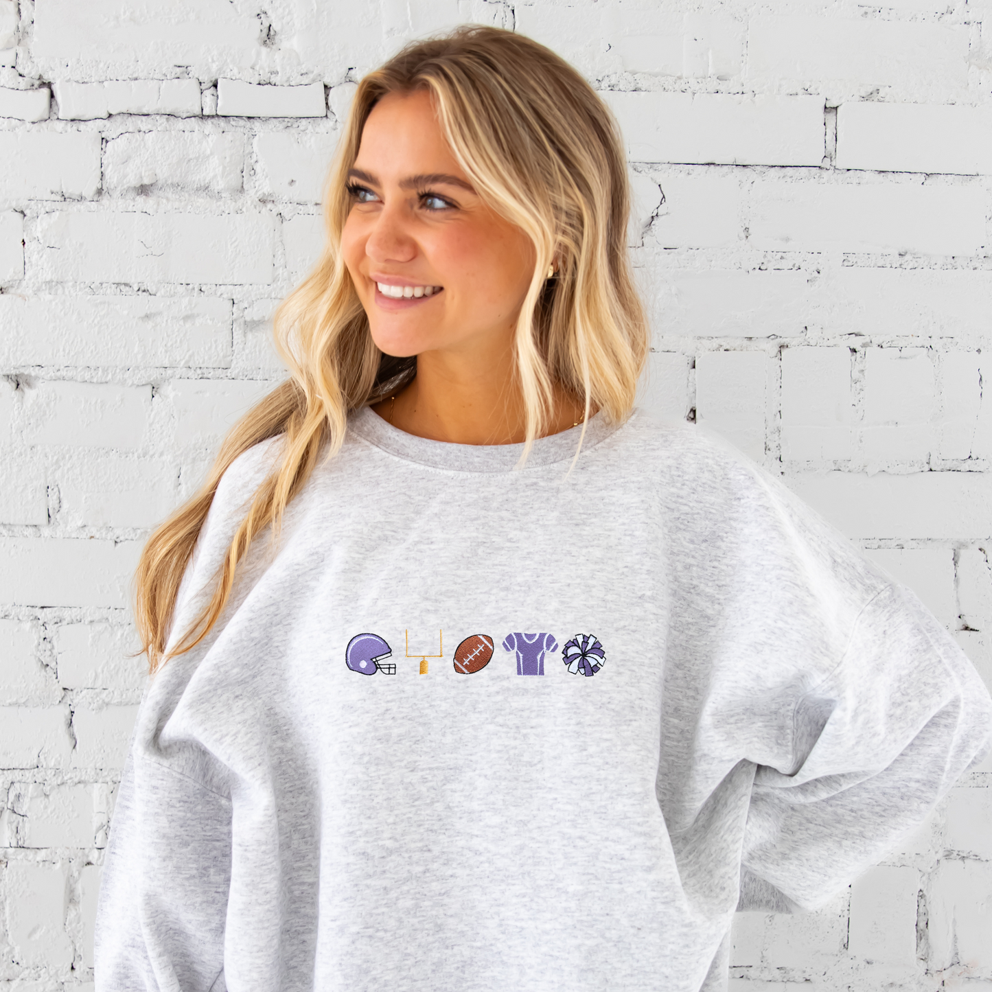 young woman wearing an ash crewneck sweatshirt with embroidered football icons in purple thread