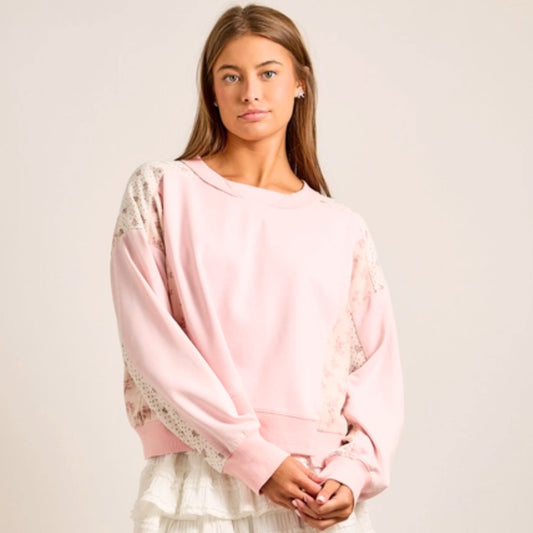 Woman wearing a pink sweater with floral patterned sleeves on a plain background