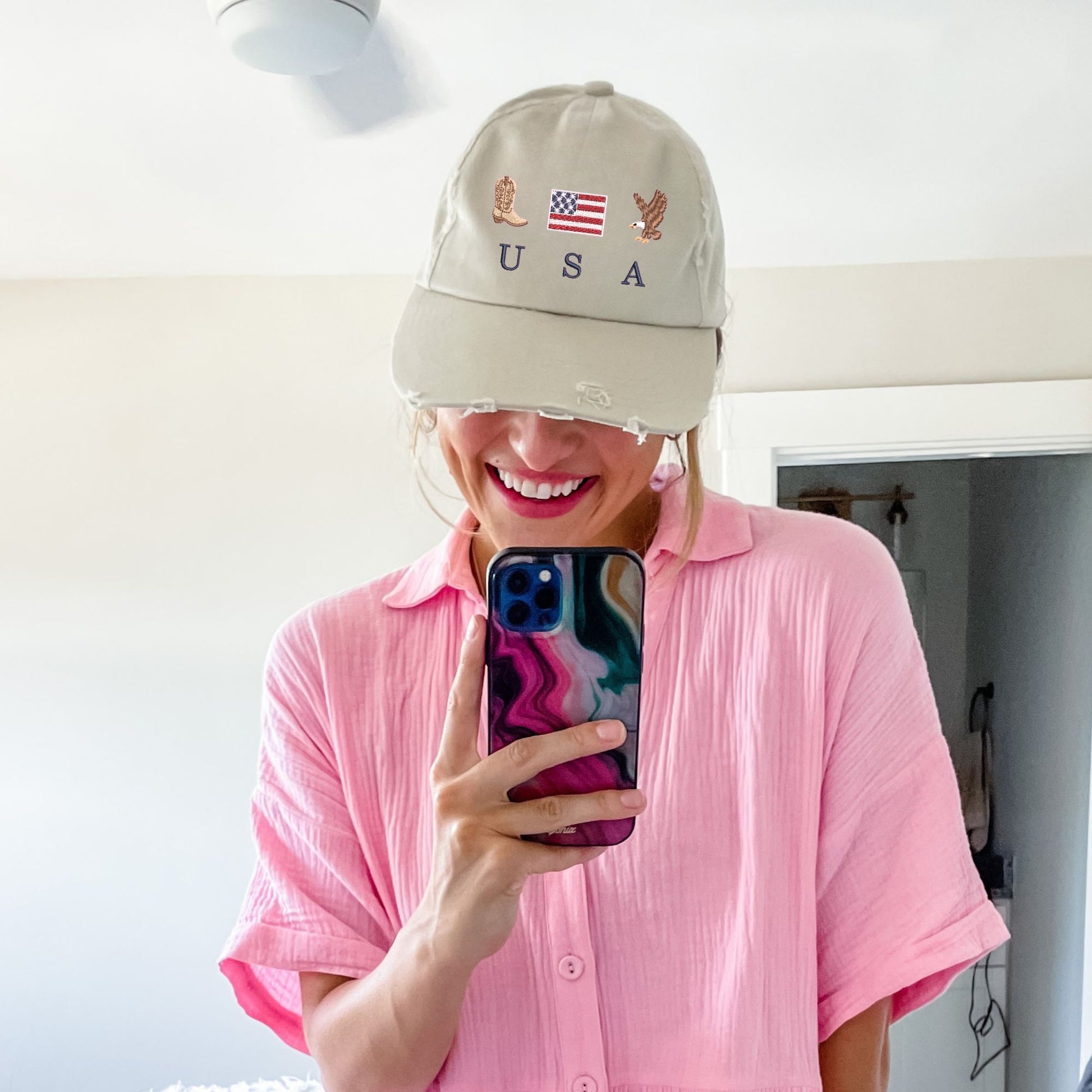 woman wearing a stone distressed baseball cap with embroidered cowboy boot, american flag, eagle, and USA design