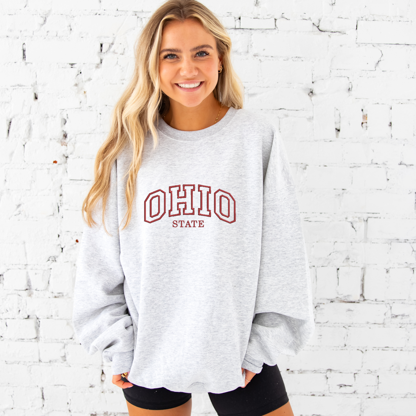 young woman wearing an ash crewneck sweathsirt with embroidered Ohio state design in red thread