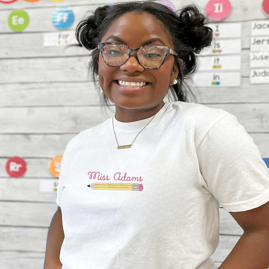 woman wearing a white comfort colors t-shirt with a custom name embroidered over a pencil icon