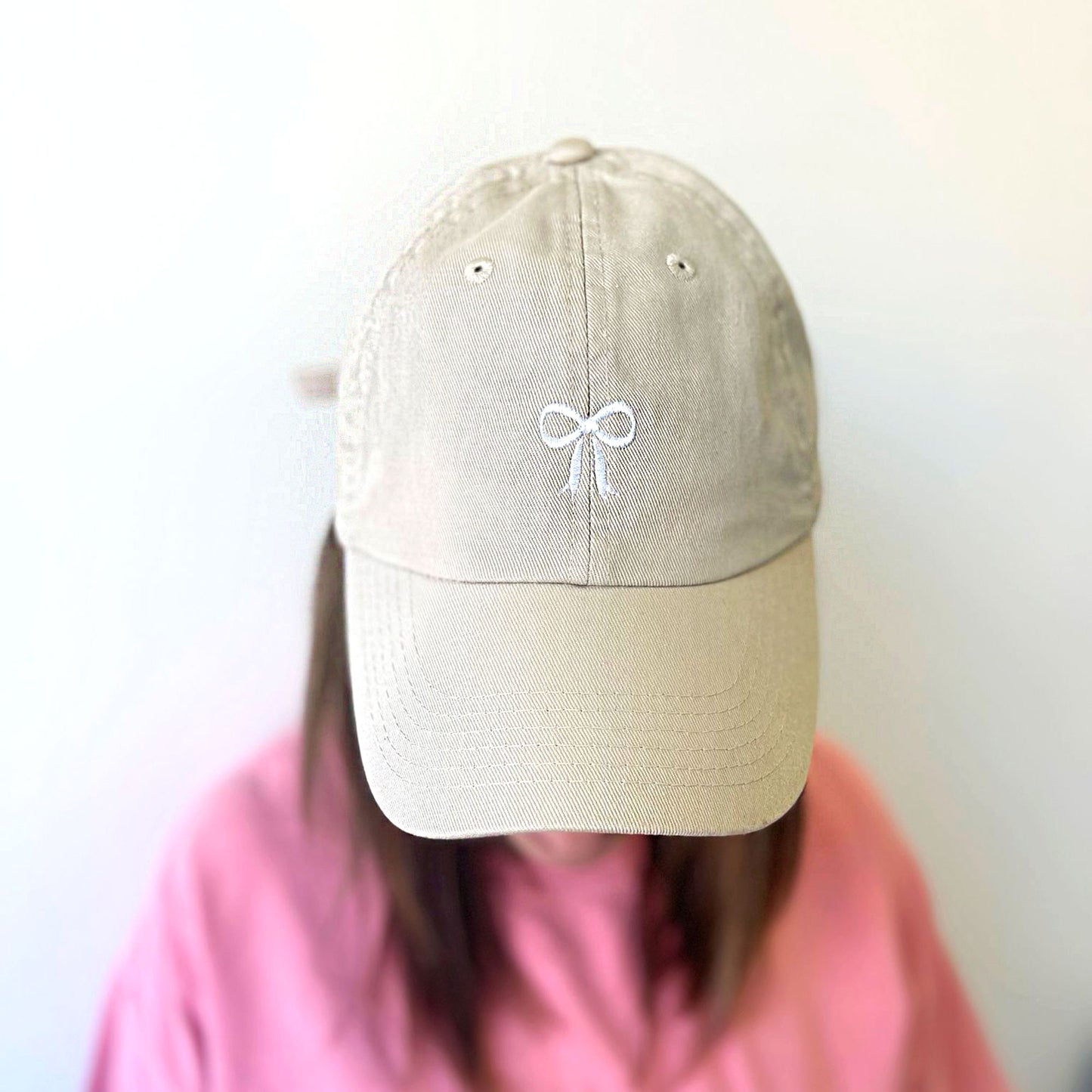 woman wearing a beige colored hat with a cute bow embroidered design