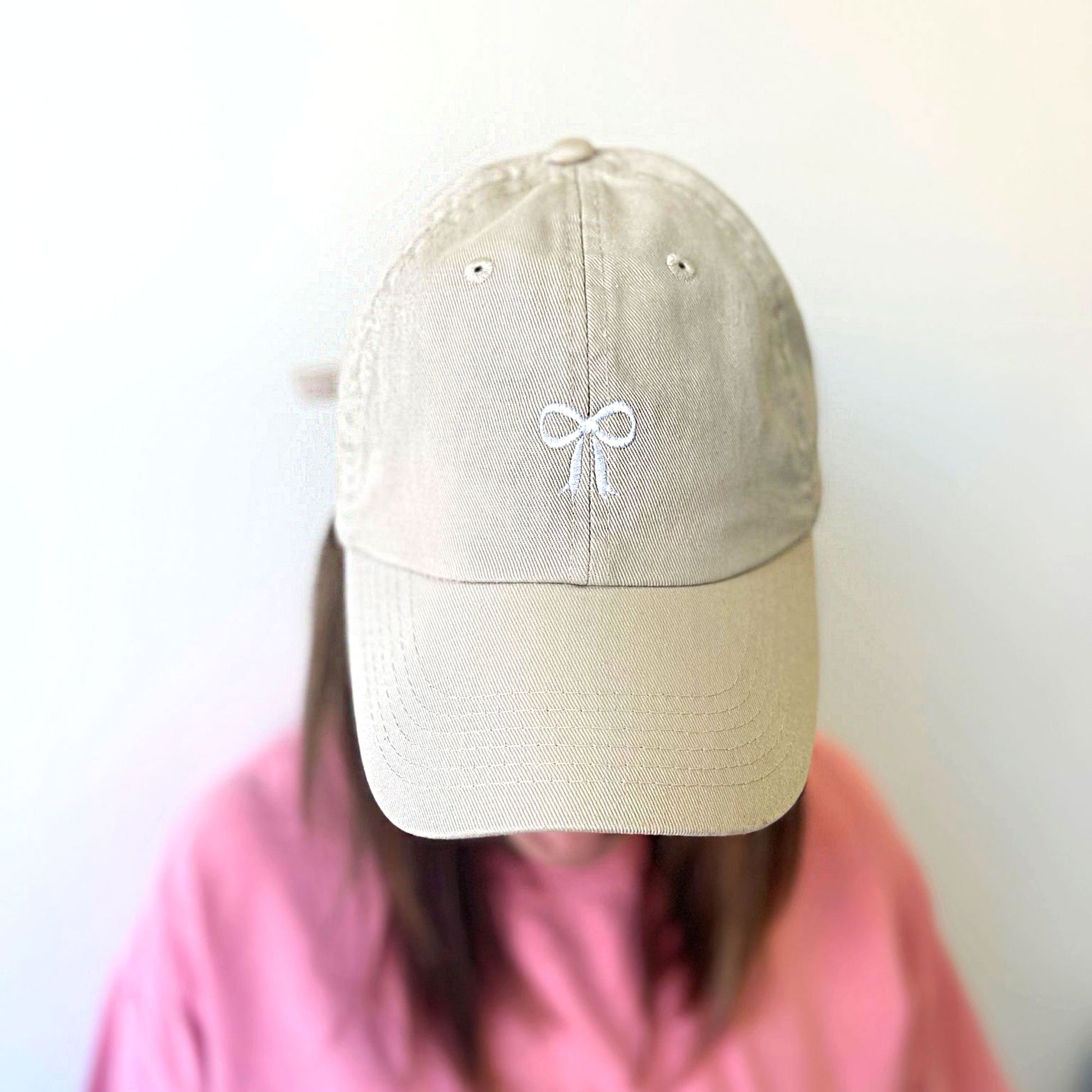 woman wearing a beige colored hat with a cute bow embroidered design