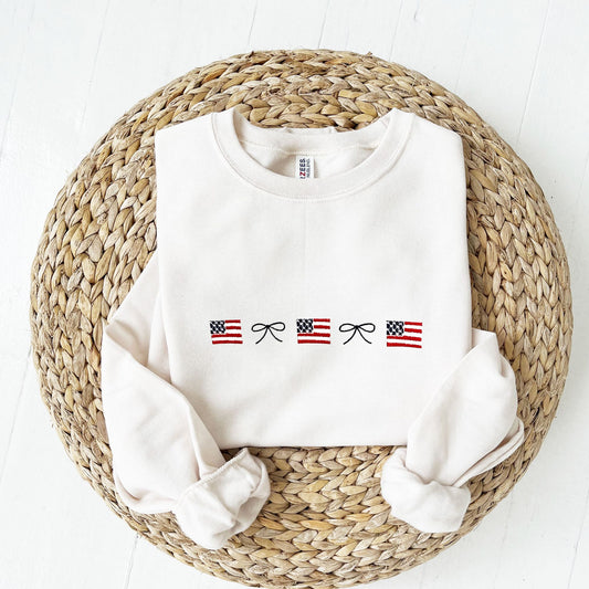 Sweet Cream crewneck sweatshirt with an embroidered dainty bow and mini USA flag alternating pattern embroidered design