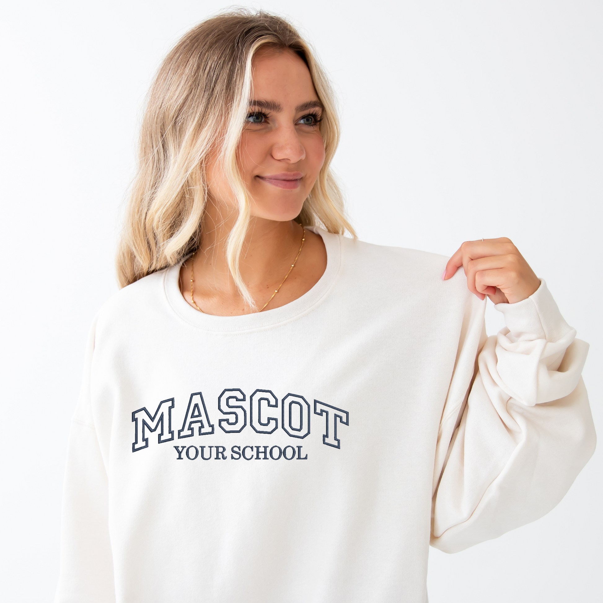 young woman wearing a sweet cream crewneck sweatshirt with custom embroidered athletic block text for mascot and school name