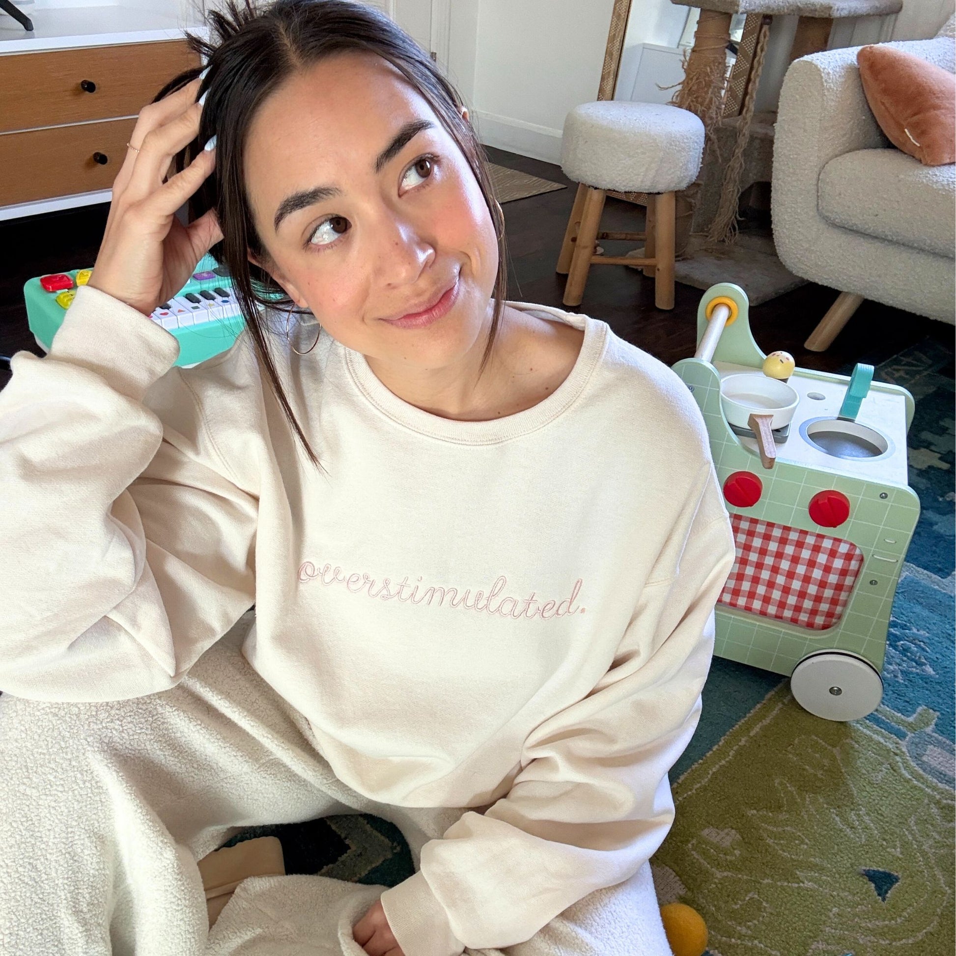 woman wearing a sweet cream crewneck sweatshirt with custom overstimulated embroidered design in a script font and powder pink thread.
