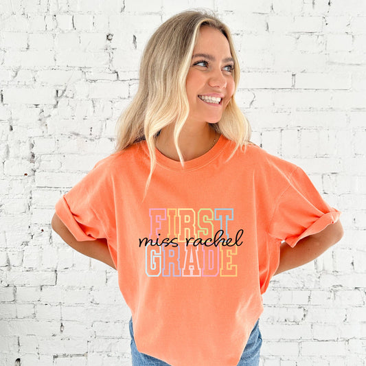 woman wearing a melon comfort colors t-shirt with a custom grade level in an open block athletic font and custom name in a script font printed on the front center