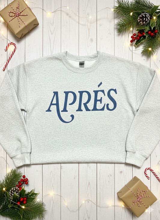 Gray sweatshirt with 'APRéS' text on a wooden surface with Christmas decorations.