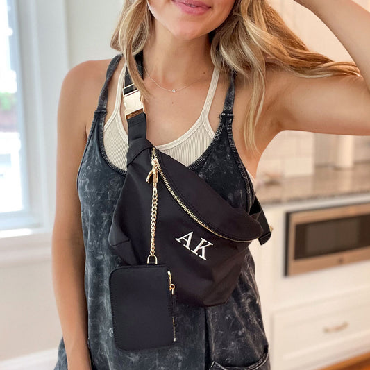 girl wearing a stylish black nylon crossbody bag with gold hardware and a clipped on wallet. main bag featuring an initial embroidery in a natural thread color.