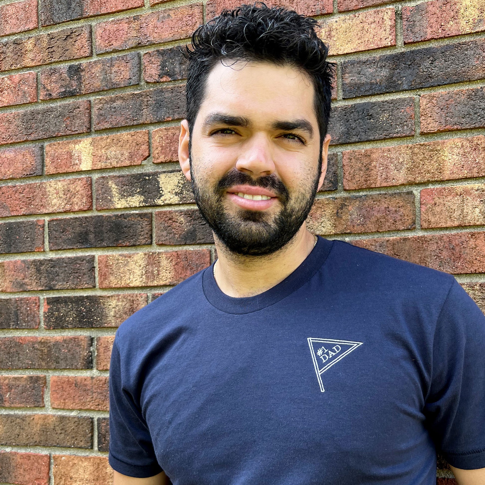 man wearing a navy crewneck tee with small embroiered pennant on the left chest that reads #1 dad