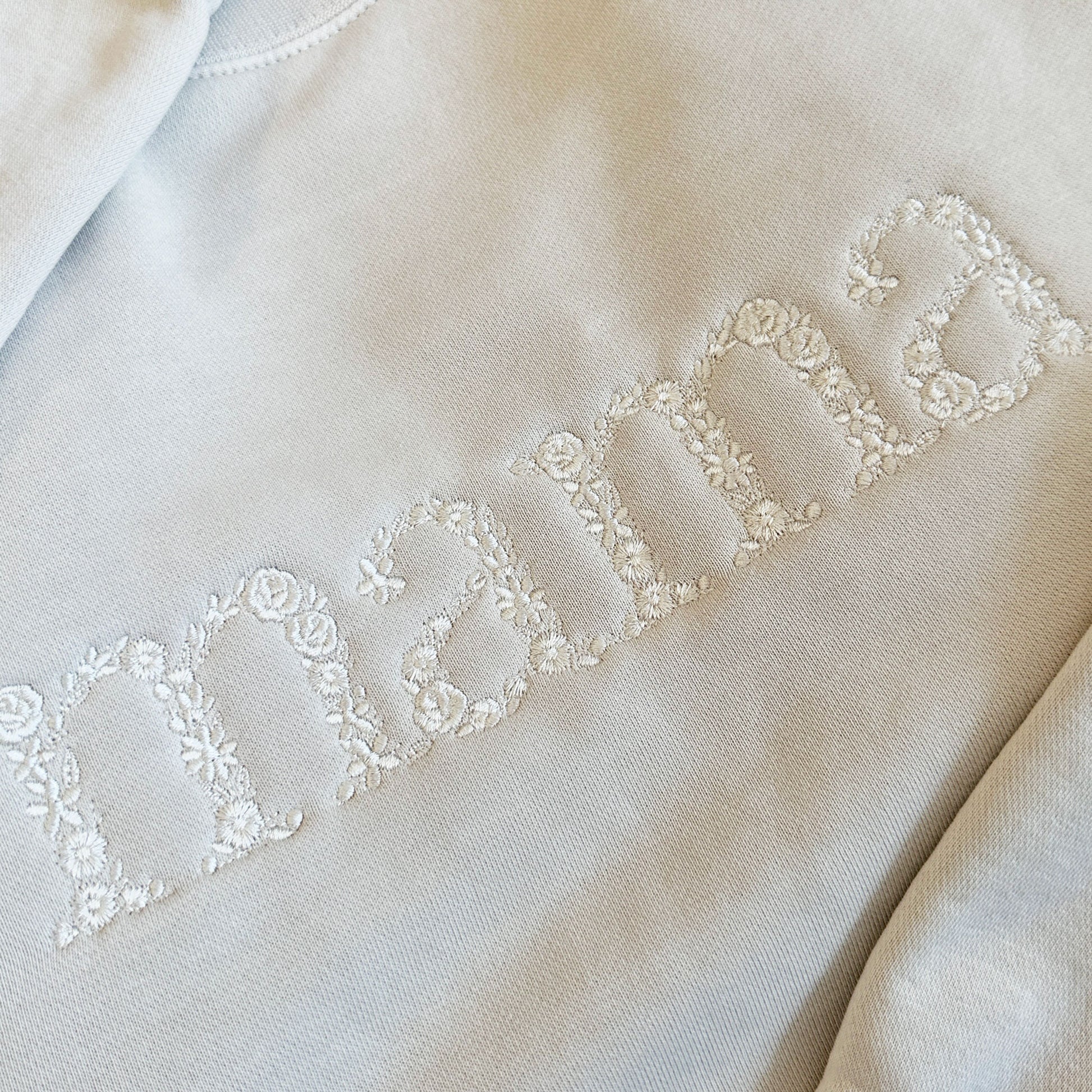 detail shot of a mama embroidered design on a sweatshirt made up of little flowers in a cream thread color