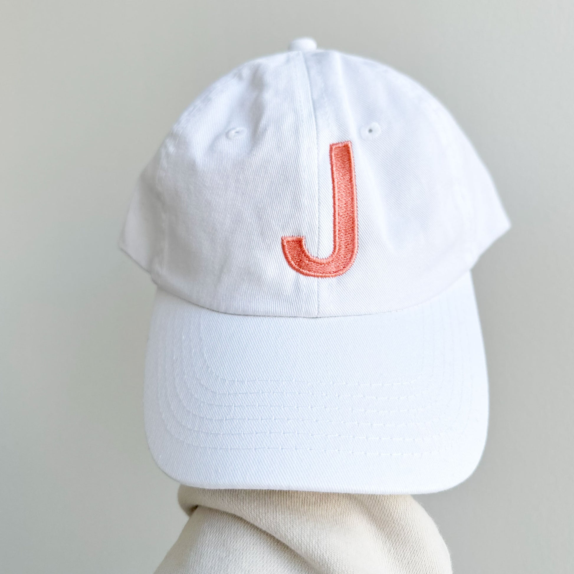 white baseball cap with a custom initial embroidery in papaya colored thread