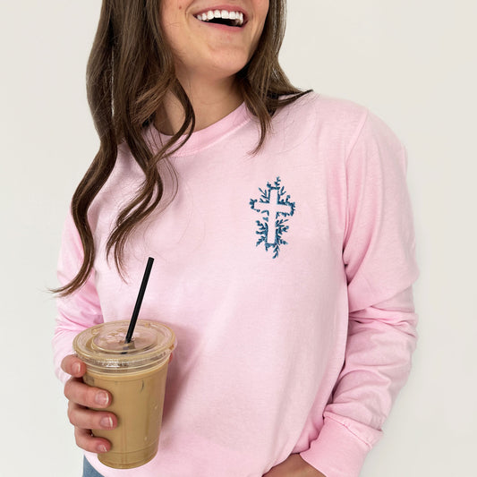 woman wearing a blossom comfort colors long sleeve shirt with a french blue flora embroidered cross on the left chest