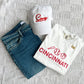 flat lay of jeans, a ehitr baseball icons print tee and an embroidered white  hat with cincy in red