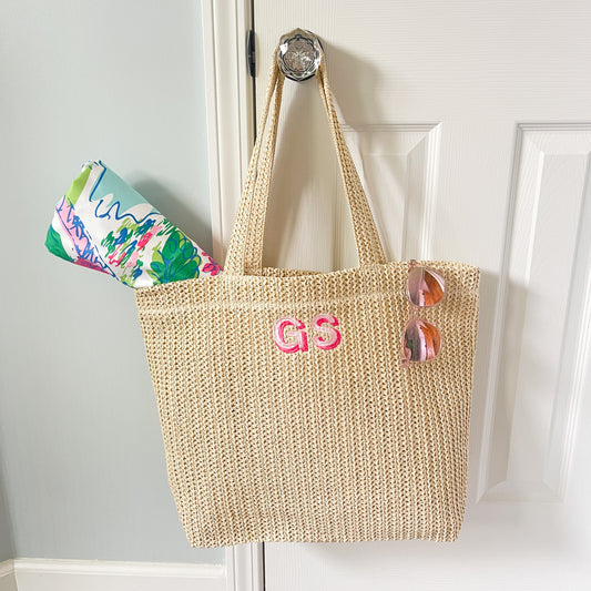 crochet straw beige bag with custom embroidered two letter block monogram in shades of pink hanging on a door handle