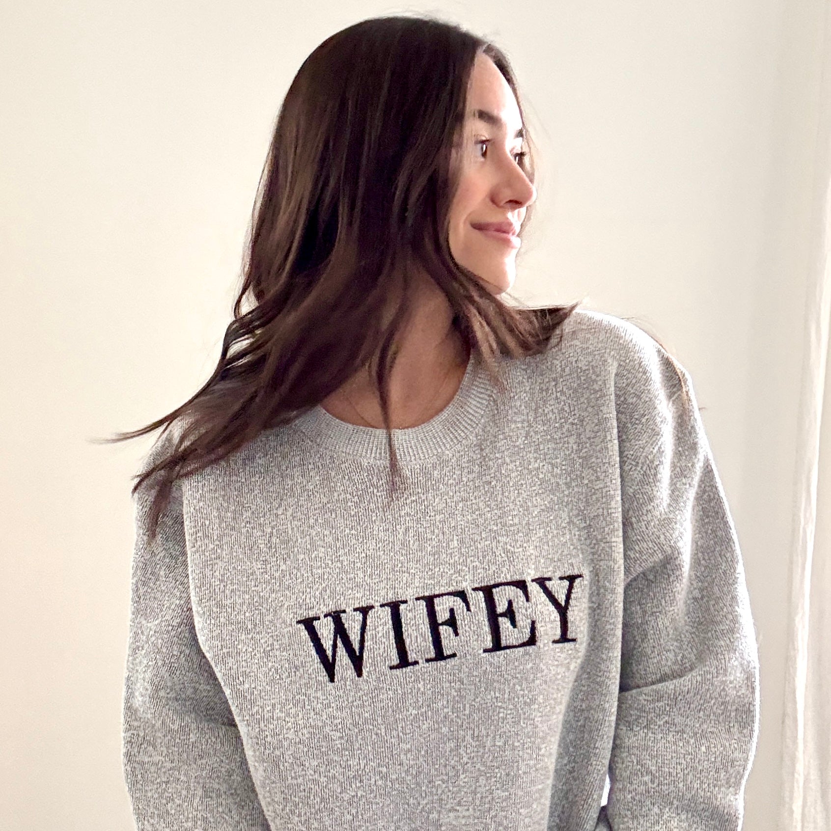 woman wearing a cozy salt and pepper knit crew with wifey embroidered across the chest in black bold letters