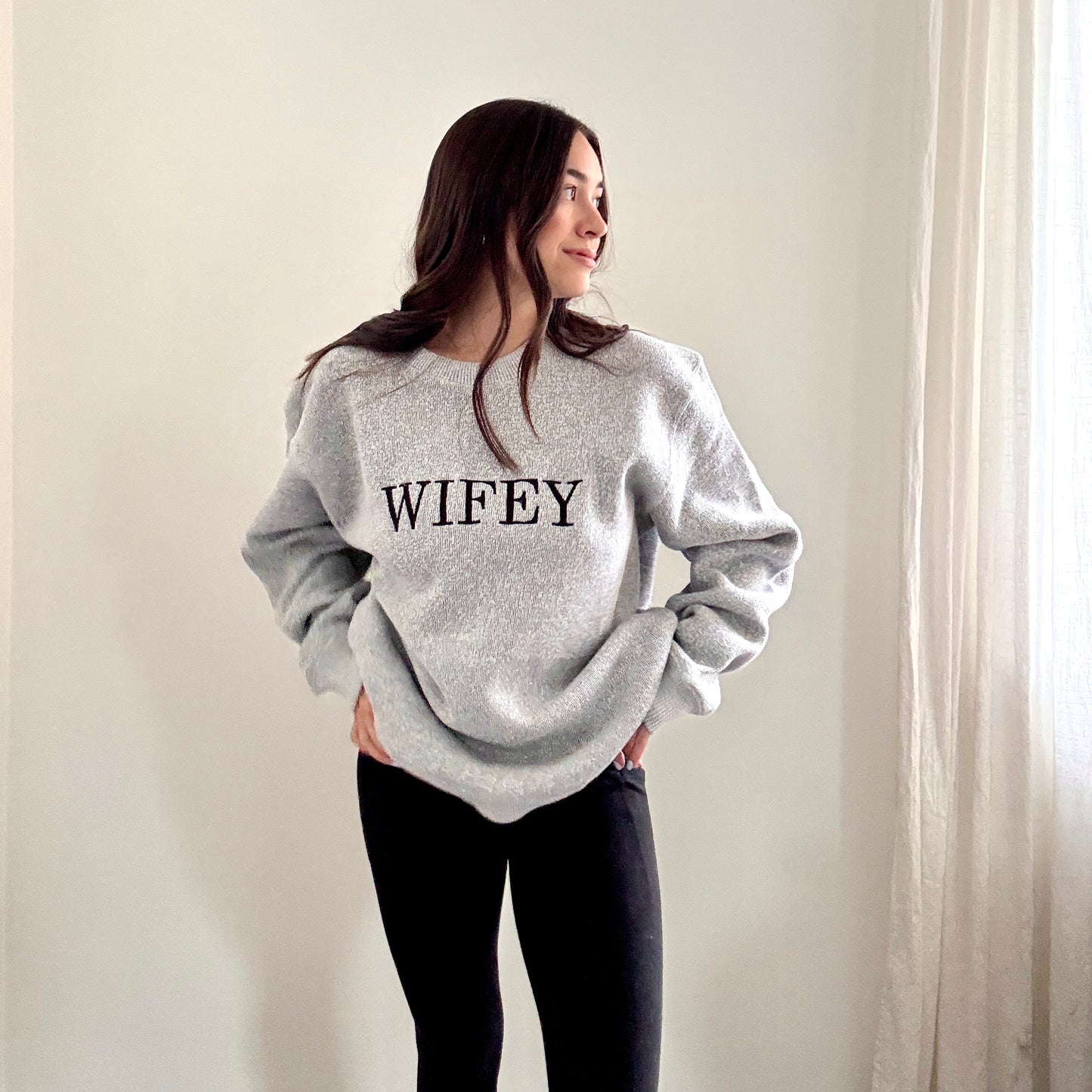 woman wearing a cozy salt and pepper knit crew with wifey embroidered across the chest in black bold letters