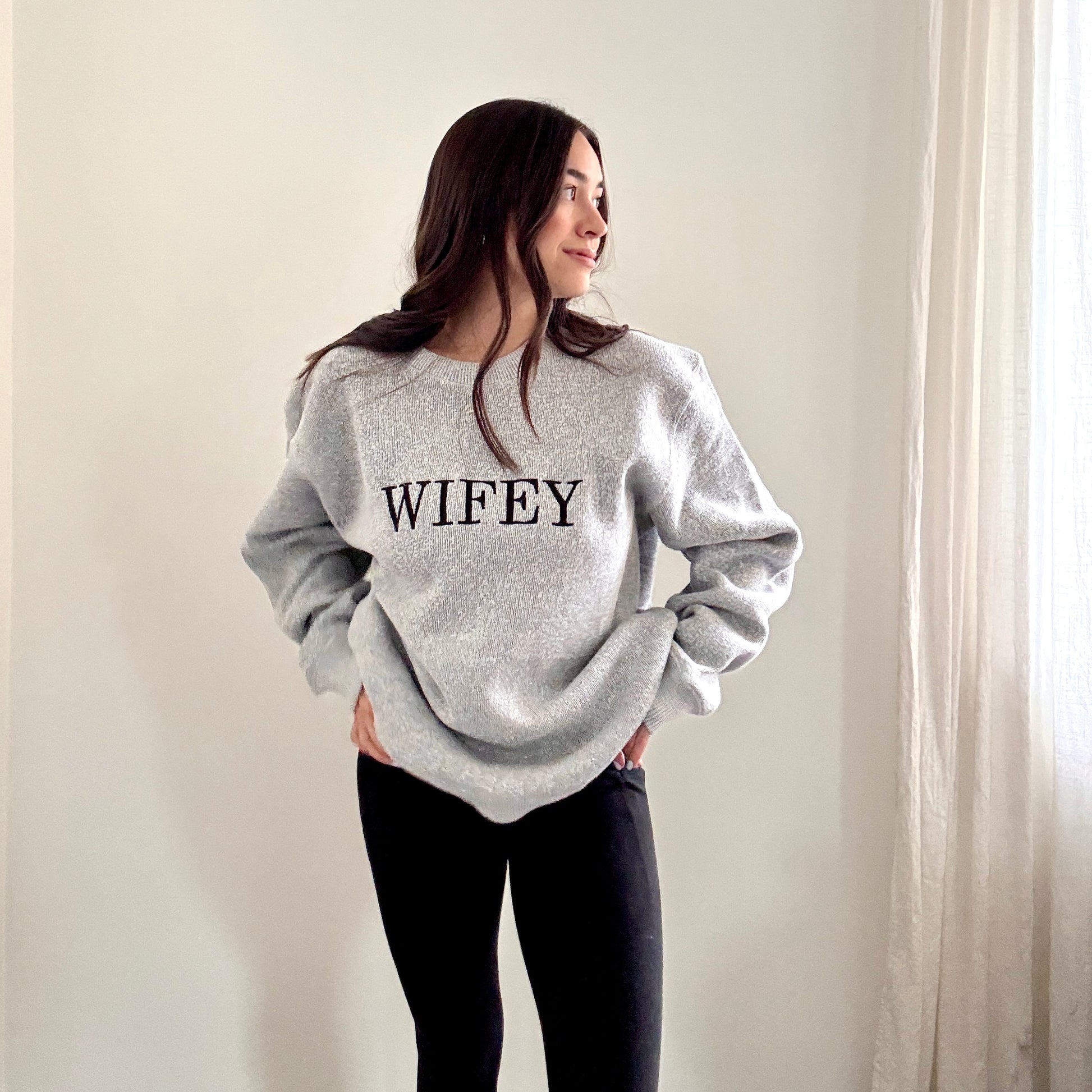woman wearing a cozy salt and pepper knit crew with wifey embroidered across the chest in black bold letters