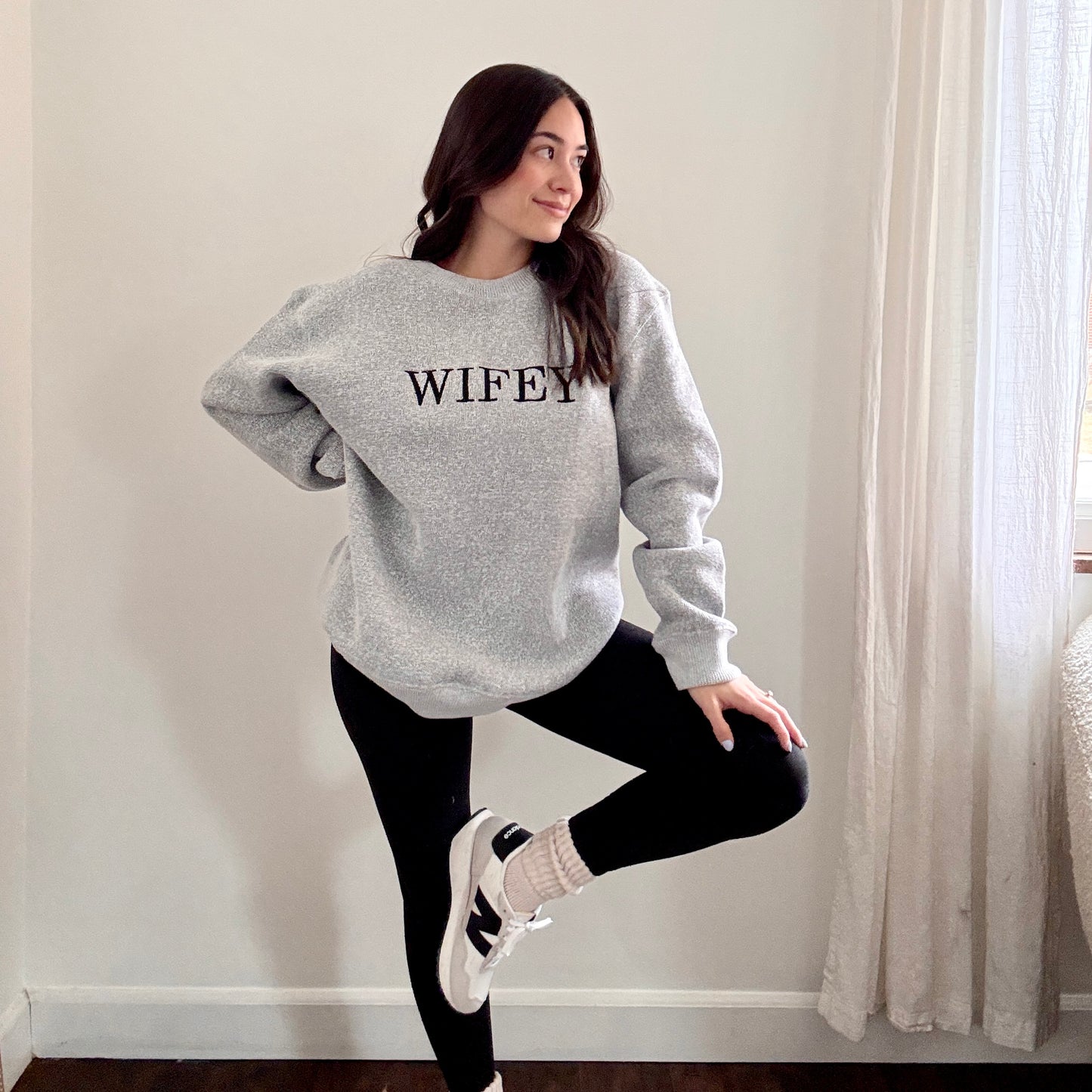 woman wearing a cozy salt and pepper knit crew with wifey embroidered across the chest in black bold letters