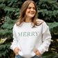 Woman wearing an embroidered MERRY crewneck sweatshirt in white. The embroidery showcases a floral Merry design in Christmas colors.