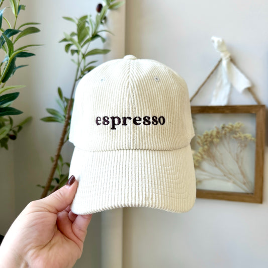 Beige corduroy cap with 'espresso' text held by a hand against a neutral background