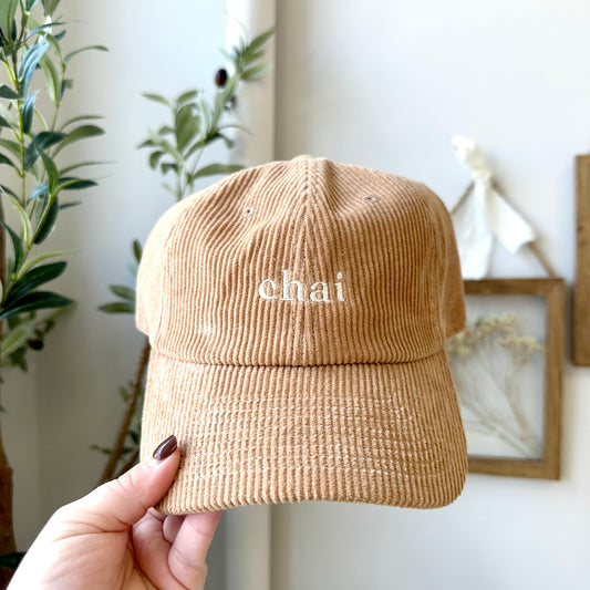 khaki corduroy cap with 'chai' embroidery held by a hand against a neutral background.