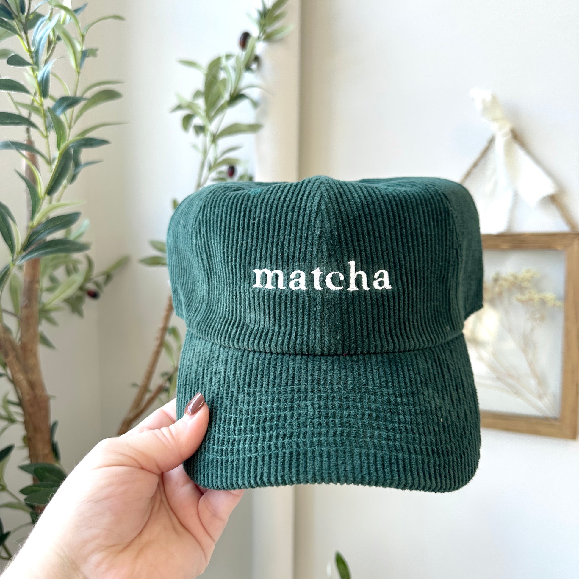 Green corduroy cap with 'matcha' text held by a hand against a neutral background