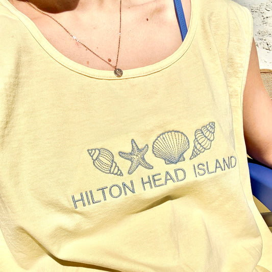 woman wearing a butter comfort colors tank top with 4 seashells and custom hilton head text embroidery design