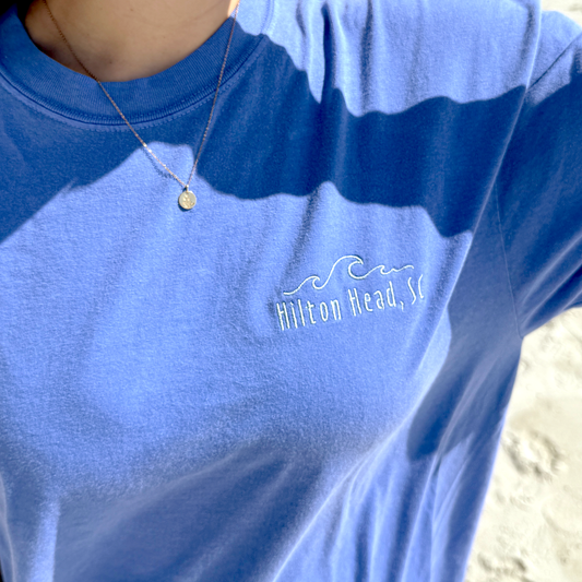close up of a girl wearing an oversized flo blue comfort colors t-shirt with custom embroidery of a wave and hilton head, sc on the left chest in powder blue thread