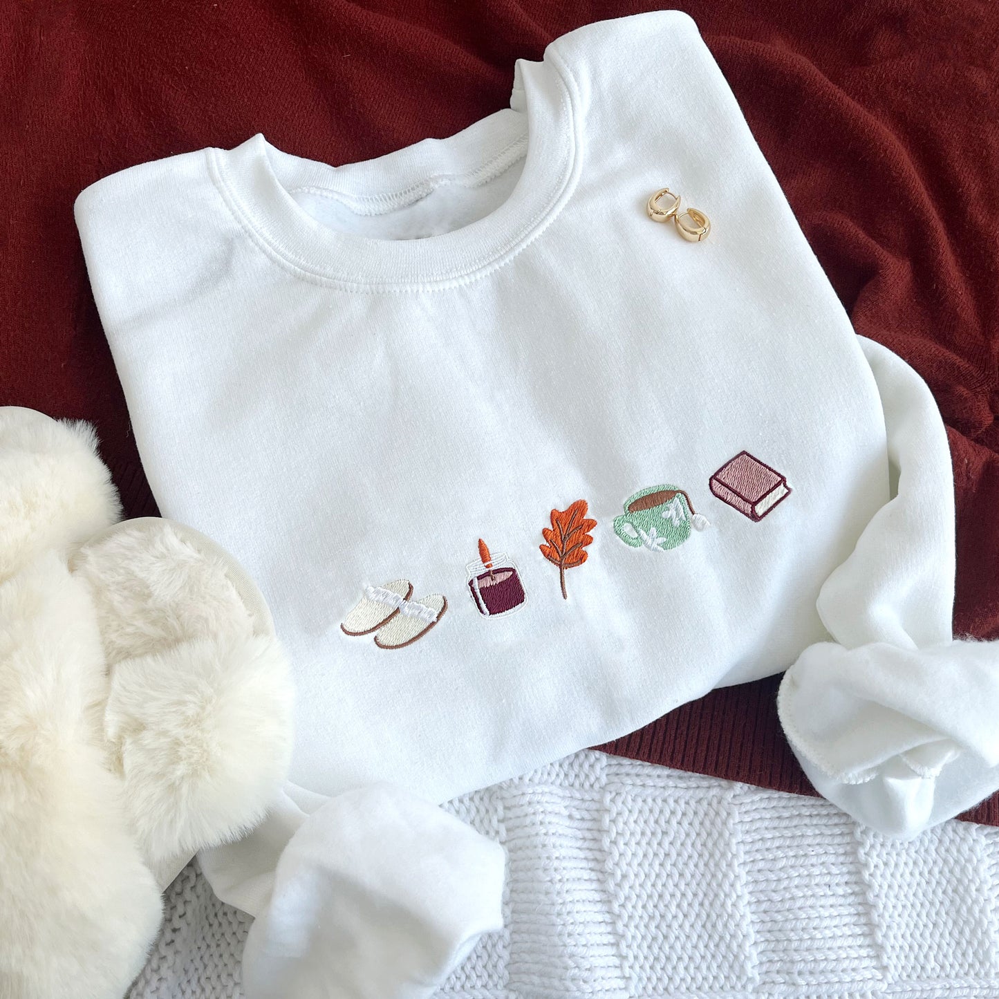 flat lay of a white crewneck sweatshirt with embroidered fall icons across the chest