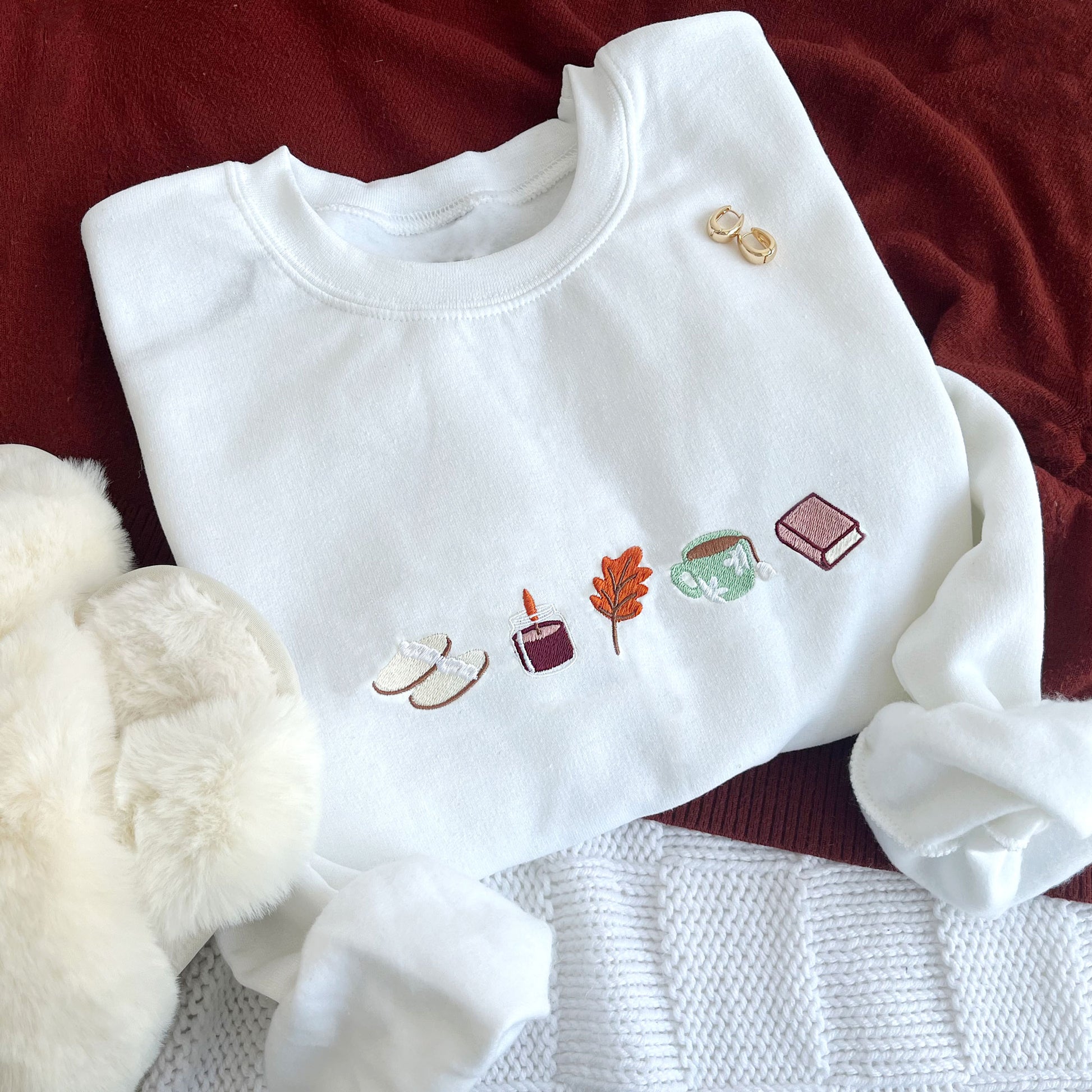 flat lay of a white crewneck sweatshirt with embroidered fall icons across the chest