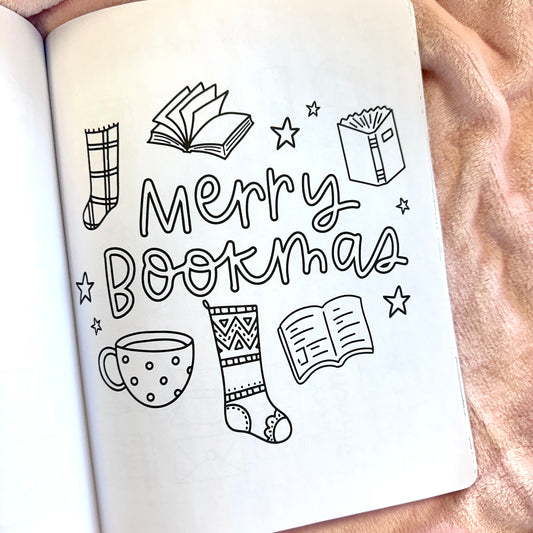 Open book with 'Merry Bookmas' text and festive illustrations on a soft fabric background